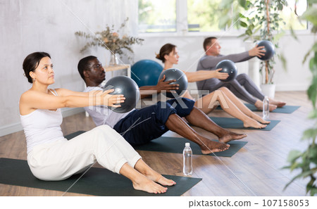 Asian woman with multiracial group doing core training with bender balls 107158053