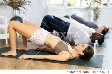 Young woman with multinational group exercising with bender balls at gym Young woman with multinational group exercising with bender balls at gym 107158201