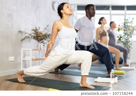 Asian woman doing Warrior Pose with hands clasped behind back in yoga studio 107158244