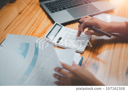 Close up Businesswoman using calculator, managing household monthly budget, summarizing taxes or bills, planning future investments, accounting bookkeeping concept. 107162308