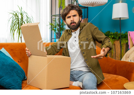 Angry dissatisfied shopper middle eastern man unpacking parcel feeling upset confused wrong delivery Angry dissatisfied shopper middle eastern man unpacking parcel feeling upset confused wrong delivery 107163869