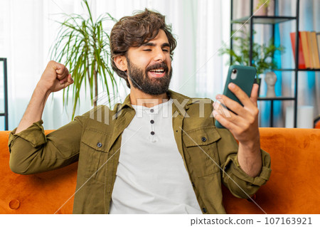 Middle eastern young man at home use smartphone celebrating success victory winning play online game 107163921