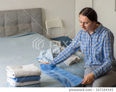 Woman folding clean terry towel in the bedroom. Organizing laundry at home. Woman folding clean terry towel in the bedroom. Organizing laundry at home. 107164345