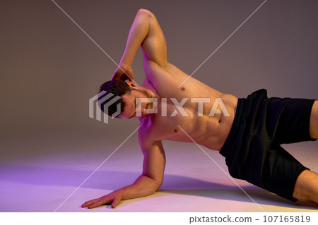 muscular bodybuilder leaning on arm and right hand while doing exercise 107165819