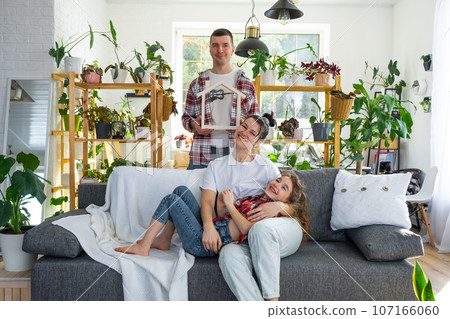 Traditional family with child are enjoying new home, sitting on the sofa and holding the roof. Mortgage, insurance and protection, buying and moving into your own home, green house with potted plant 107166060