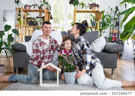 Traditional family with child are enjoying new home, sitting on the sofa and holding the roof. Mortgage, insurance and protection, buying and moving into your own home, green house with potted plant Traditional family with child are enjoying new home, sitting on the sofa and holding the roof. Mortgage, insurance and protection, buying and moving into your own home, green house with potted plant 107166077