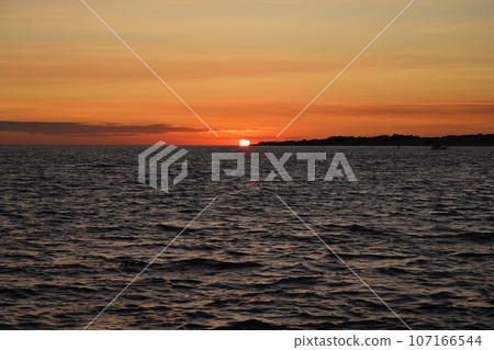 Beautiful colourful sunset on the beach with the sea and waves. A concept for travel, holidays and summer holidays by the sea. Greece - Corfu island - Agios Georgios. Beautiful colourful sunset on the beach with the sea and waves. A concept for travel, holidays and summer holidays by the sea. Greece - Corfu island - Agios Georgios. 107166544