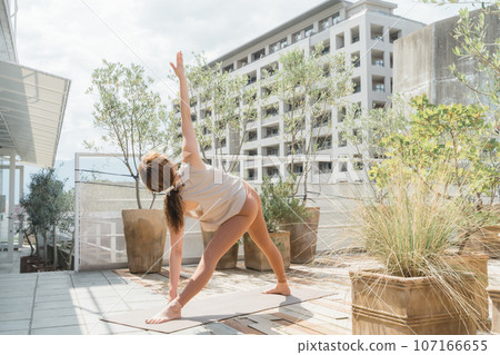 A woman doing yoga/Pilates on the roof of an apartment in the city (triangle pose) A woman doing yoga/Pilates on the roof of an apartment in the city (triangle pose) 107166655