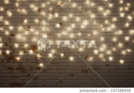 Minimalist white brick wall adorned with shimmering Christmas lights, perfect for background. 107166936