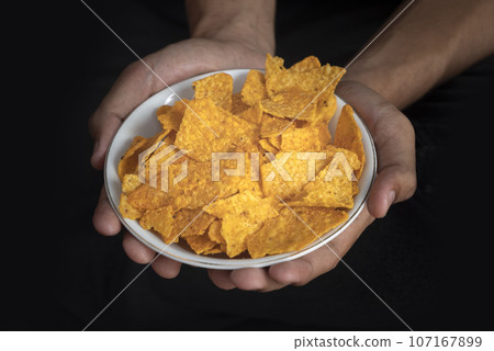 A human hand holding a plate with tortilla chips 107167899