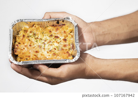 A human hand holding pasta macaroni schotel in an aluminum foil cup 107167942