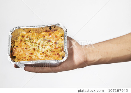 A human hand holding pasta macaroni schotel in an aluminum foil cup 107167943