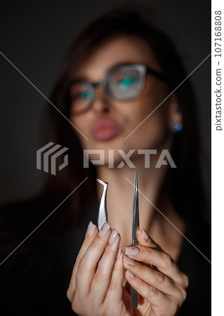 beautiful woman holding eyelashes tweezers on black background 107168808