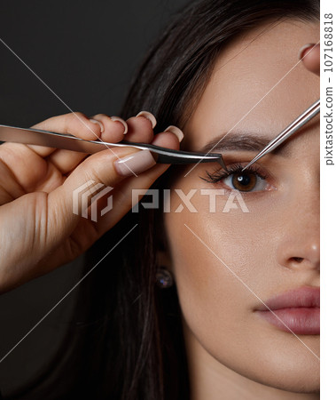 beautiful woman holding eyelashes tweezers on black background beautiful woman holding eyelashes tweezers on black background 107168818