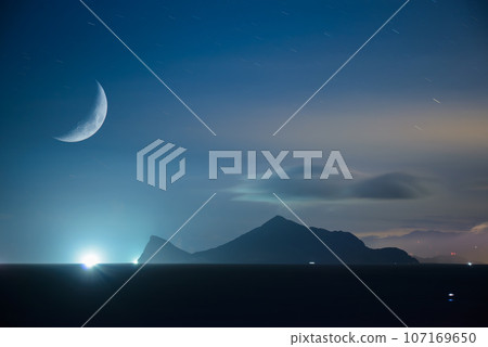 A poetic half-moon montage of fishing boat lights on the shore of an island. 107169650