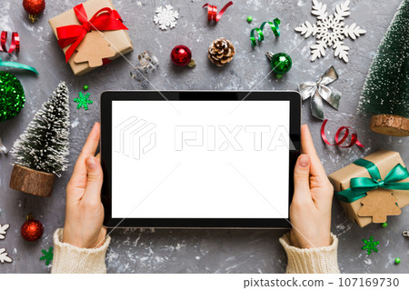 Christmas online shopping from home, female hands holding tablet pc with blank white display top view. woman hand holding tablet with blank screen, Christmas tree and gifts on background Christmas online shopping from home, female hands holding tablet pc with blank white display top view. woman hand holding tablet with blank screen, Christmas tree and gifts on background 107169730