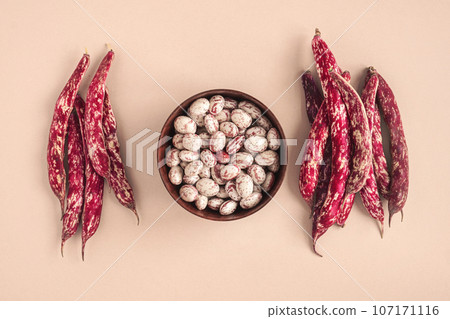 Cranberry beans. Borlotti bean pods in bowl. Top view. Stylish modern food background. Magenta color. Creative foodstuff flat lay. Grocery, dietary backdrop. Advertising, trendy magazine publication. 107171116