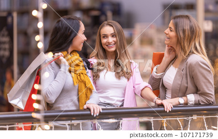 Three happy female friends are talking about their purchases in the mall 107171739