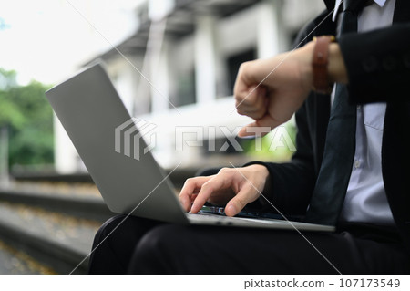 Cropped shot of businessman using laptop and checking time on wristwatch for appointment or transportation 107173549
