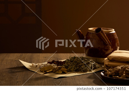 Porcelain pot with paper prepared to wrap herbs into medicine packets decorated on wooden table and brown background. Medicines originating from ancient China, health-protecting foods 107174351
