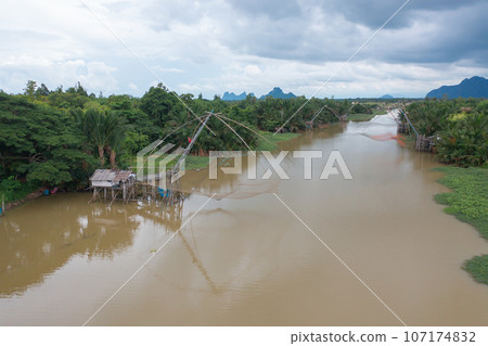 Aerial view of fishing trap net in canel with fisherman urban city village town houses, lake or river. Nature landscape fisheries and fishing tools at Pak Pha, Songkhla, Thailand. Aquaculture farming Aerial view of fishing trap net in canel with fisherman urban city village town houses, lake or river. Nature landscape fisheries and fishing tools at Pak Pha, Songkhla, Thailand. Aquaculture farming 107174832