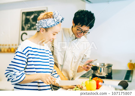 一對夫婦一邊做菜一邊看智慧型手機 107175807