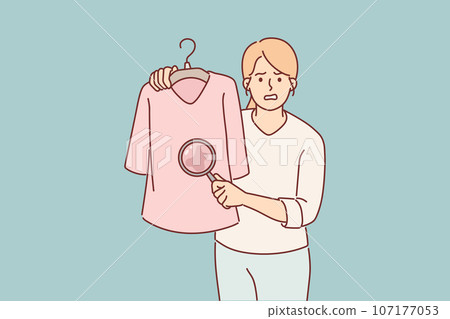 Woman shows stain on t-shirt under magnifying glass and needs to use laundry detergent Woman shows stain on t-shirt under magnifying glass and needs to use laundry detergent 107177053