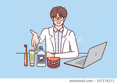 Man dentist pulls hand to screen, sitting at table with laptop and supplies for dental care Man dentist pulls hand to screen, sitting at table with laptop and supplies for dental care 107178271