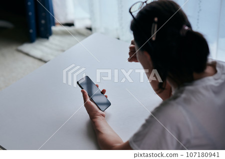 Senior woman holding a smartphone and holding her eyebrows Senior woman holding a smartphone and holding her eyebrows 107180941
