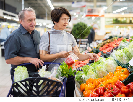 Smiling happy couple is choosing bell peppers and other vegetables in supermarket Smiling happy couple is choosing bell peppers and other vegetables in supermarket 107181885