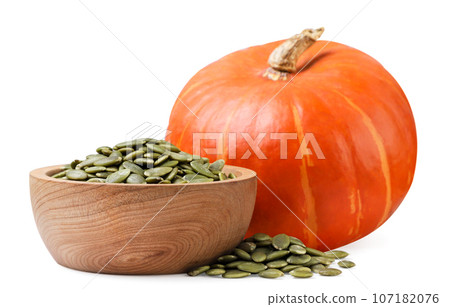 Pumpkin seeds in a wooden plate and scattered close-up on a white background. 107182076