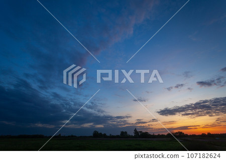 View of evening clouds and sky after sunset over a meadow 107182624