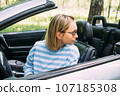 A woman is driving a convertible car. Summer road trip to nature 107185308