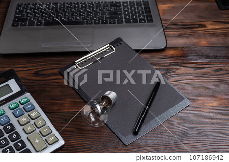 Use of electricity at home. Incandescent lamp on the table near the computer. Tablet and pen. Use of electricity at home. Incandescent lamp on the table near the computer. Tablet and pen. 107186942