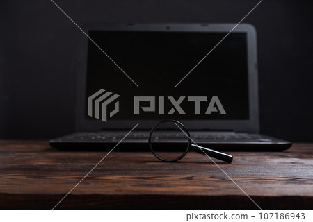 Magnifying glass on the background of a laptop. Search for information on the Internet. 107186943