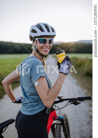 Diabetic cyclist with a continuous glucose monitor on her arm drinking water during her bike tour. Diabetic cyclist with a continuous glucose monitor on her arm drinking water during her bike tour. 107186995