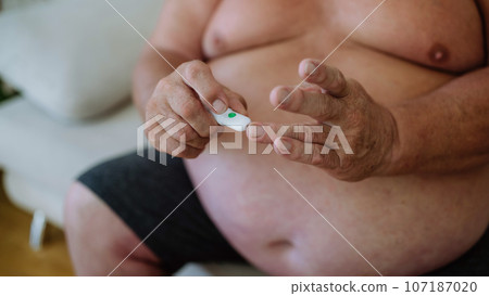 Overweight man checking blood glucose level at home using a fingerstick glucose meter. 107187020