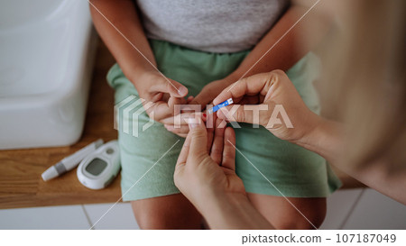 Mother checking her son's blood glucose level at home using a fingerstick glucose meter. 107187049
