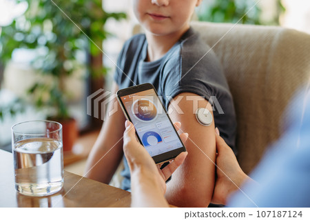 Girl with diabetes checking blood glucose level at home using continuous glucose monitor. 107187124