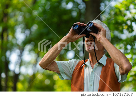Senior man spending free time outdoors in nature, watching forest animals through binoculars. Senior man spending free time outdoors in nature, watching forest animals through binoculars. 107187167