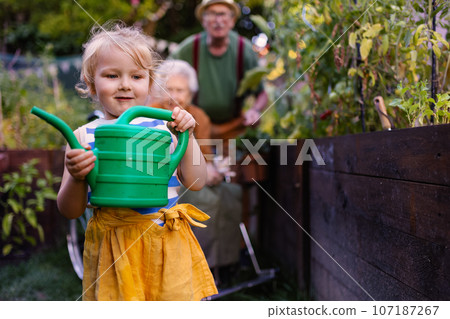Portrait of a little adorable girl helping her grandparents in the garden. 107187267