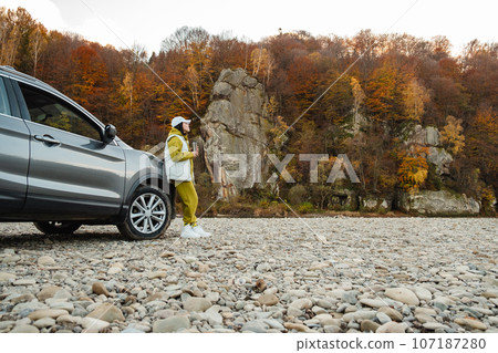 woman standing near car drinking tea looking at mountain river 107187280