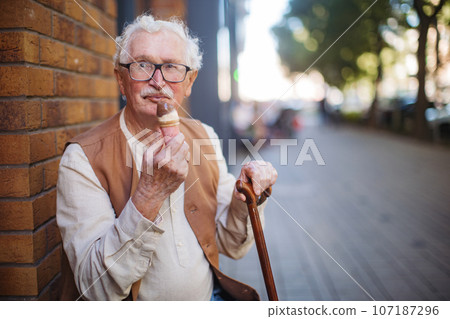 Portrait of senior man with walking cane, eating ice cream on a hot summer day. 107187296