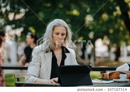 Portrait of beautiful female manager in middle age with gray hair working outdoors. Portrait of beautiful female manager in middle age with gray hair working outdoors. 107187314