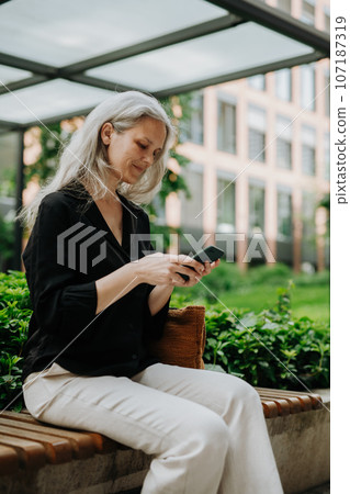 Portrait of beautiful woman with gray hair sitting on bench in city. 107187319