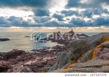 Road to La Corbiere lighthouse on the sea bottom in a low tide with cliff and sunset, bailiwick of Jersey, Channel Islands, Great Britain Road to La Corbiere lighthouse on the sea bottom in a low tide with cliff and sunset, bailiwick of Jersey, Channel Islands, Great Britain 107187370