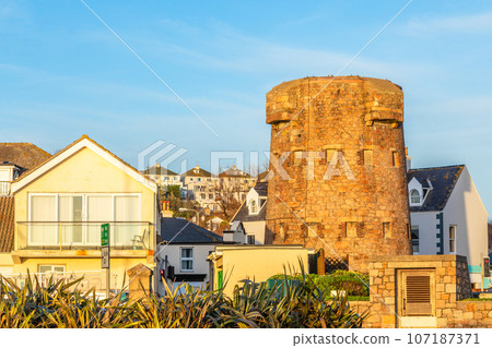 First tower of round coastal defence line with residential district in the background, bailiwick of Jersey, Channel Islands, Great Britain 107187371