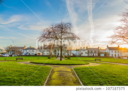 Green park with small white houses along the road on the sunset, Belozanne, Saint Helier, bailiwick of Jersey, Channel Islands, Great Britain Green park with small white houses along the road on the sunset, Belozanne, Saint Helier, bailiwick of Jersey, Channel Islands, Great Britain 107187375