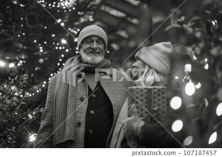Black and white portrait of senior couple enjoying christmas market, buying gifts and christmas tree. Black and white portrait of senior couple enjoying christmas market, buying gifts and christmas tree. 107187457