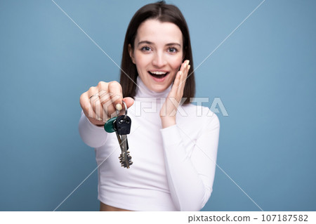 Portrait of a happy woman with keys in her hands on a blue plain background in the studio. Buying or renting a home 107187582